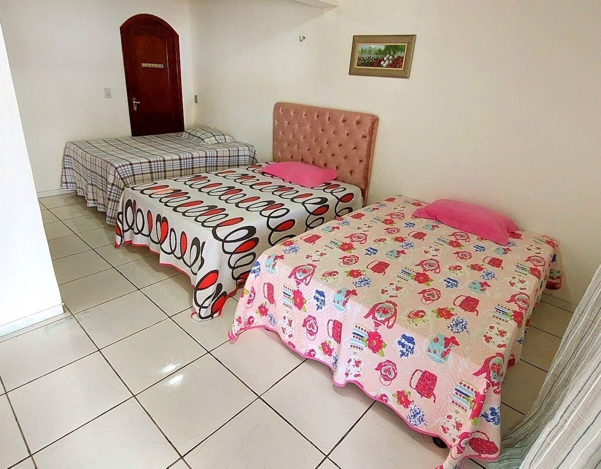 A room with two beds, each with a distinct patterned bedspread, a wooden door, and a framed picture on the wall.