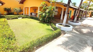 A courtyard with a well-maintained lawn, palm trees, and a yellow building with arches. - Aconchego do Caranã (Salinópolis)