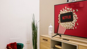 Un salon moderne avec un téléviseur, un panneau rouge sur lequel on peut lire « NETFLIX », une plante, un panier et un meuble en bois.