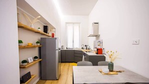 Une cuisine compacte comprenant un réfrigérateur, des étagères en bois, une table à manger avec des chaises et un îlot de cuisine.