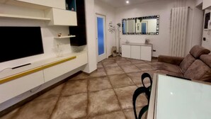 Una sala moderna con un televisor de pantalla plana montado en la pared, una consola blanca, un sofá marrón y un espejo grande sobre la consola.