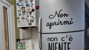 Una cocina con un refrigerador de acero inoxidable, una repisa montada en la pared con imanes y un armario blanco debajo.