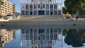 Un edificio moderno con fachada simétrica y entrada central, reflejado en aguas tranquilas.