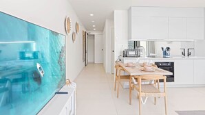 A modern kitchen with white cabinets, a dining area with a wooden table and chairs, and a large glass fish tank on the left. - B254 - Cozy Apartment in the Heart of Simpson Bay (Sint Maarten)
