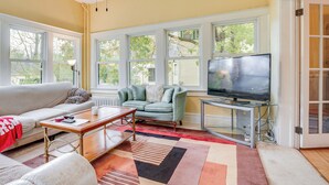 Ein Wohnzimmer mit einer Couch, einem Couchtisch, einem Fernseher und einem Fenster mit Blick auf Bäume.