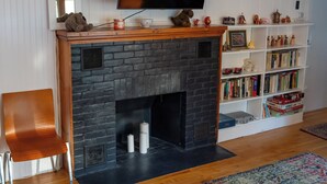 Una sala de estar con chimenea, un televisor montado encima, una estantería llena de libros y un sillón.