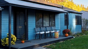 Una casa azul con porche, chimenea y un pequeño jardín con calabaza y flores.