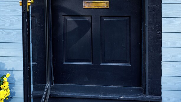 Una puerta principal negra con un aldabón de bronce, una ranura para correo y una cerradura.