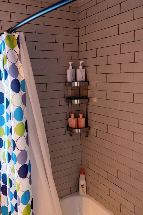 Ein Badezimmer mit Duschvorhang, Ablagefläche für Pflegeprodukte und einer Shampoo-Flasche.