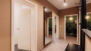 A hallway with a large mirror, a coat rack, and a bench. - Luga Homes - Karli (Leipzig)