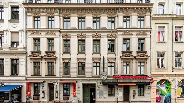 A multi-story building with a row of shops on the ground floor, including a restaurant named "Hopperpower". - Luga Homes - Karli (Leipzig)