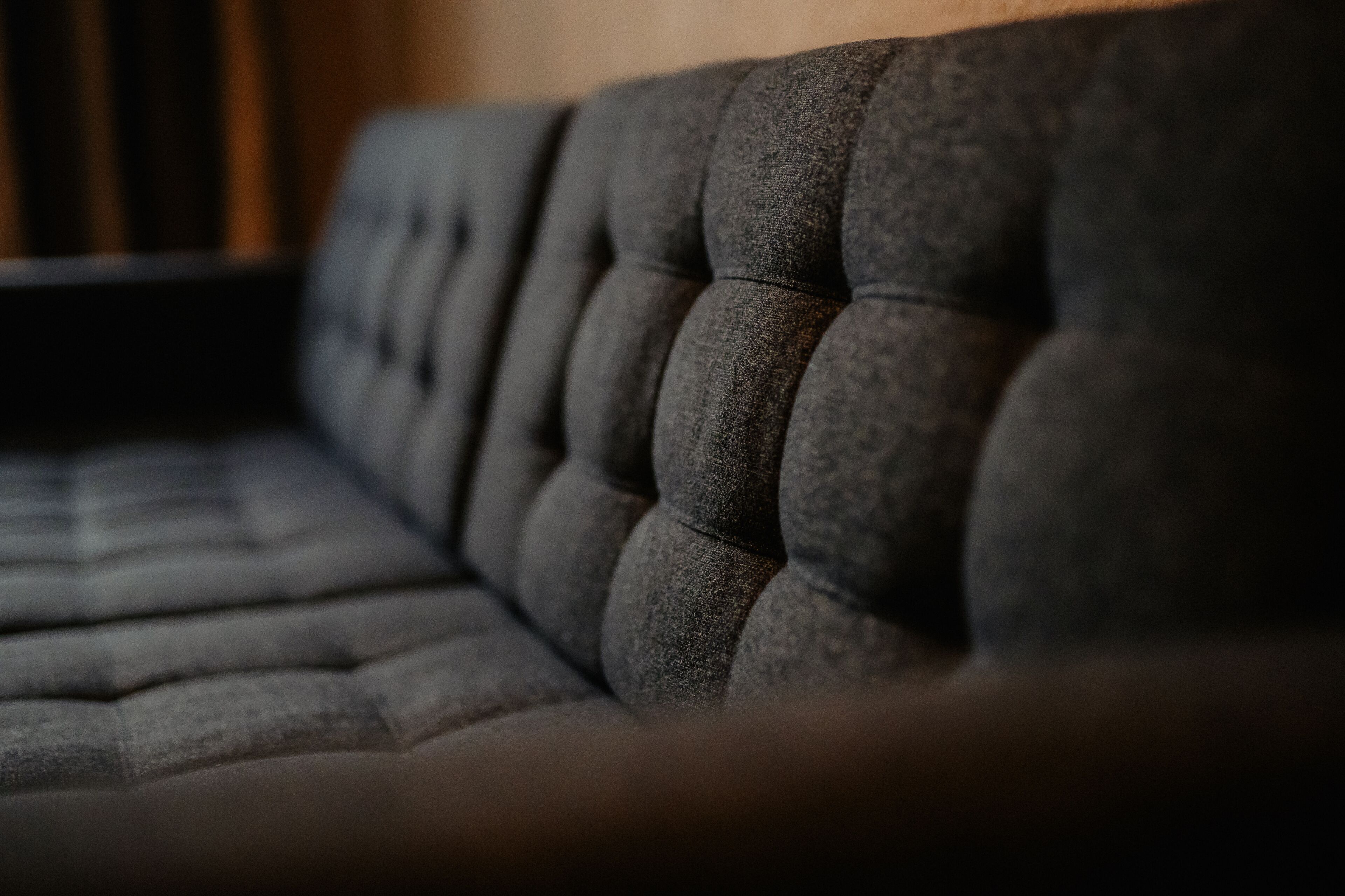 A close-up of a dark, tufted sofa with a smooth, upholstered texture.