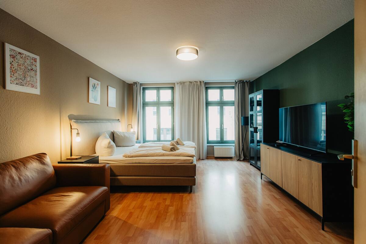 Una habitación de hotel moderna con sofá, cama, televisión y ventanas amplias.
