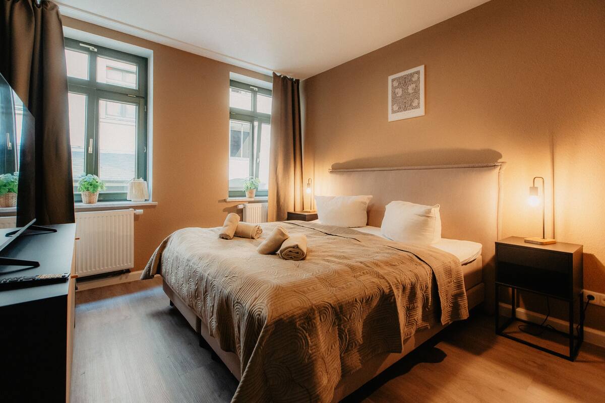 Habitación de hotel con una cama grande, mesitas de noche, un escritorio y una ventana con cortinas.