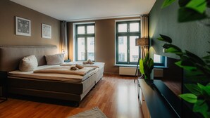 A modern bedroom with a large bed, a flat-screen TV, and a window with curtains. - Luga Homes - Karli (Leipzig)