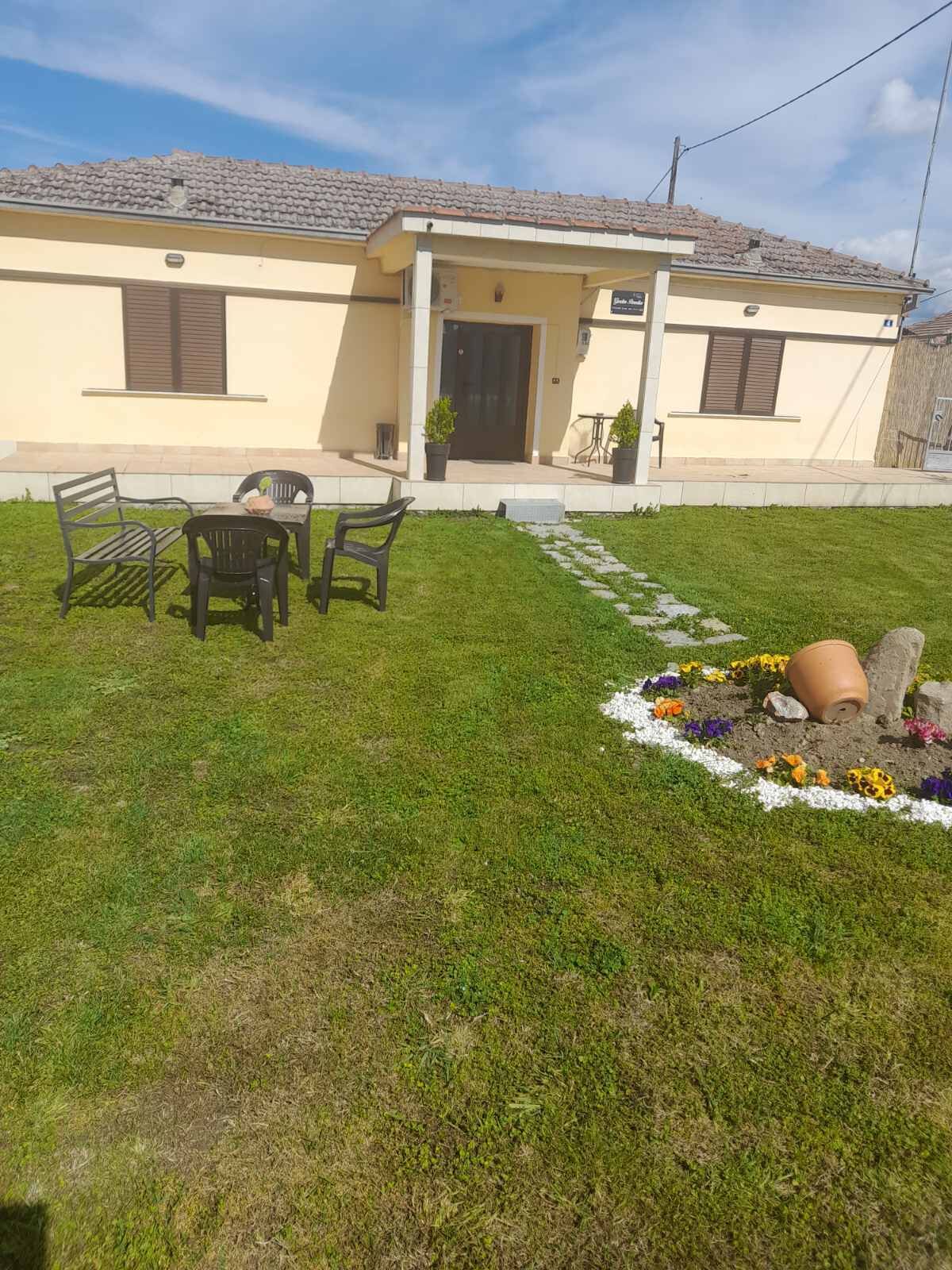A house with a front porch, a small garden with a flower bed, and a table and chairs outside.