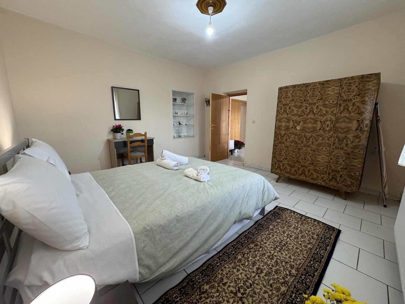 A bedroom with a bed, a bedside table with a lamp, a chair, a wardrobe, and a mirror on the wall.