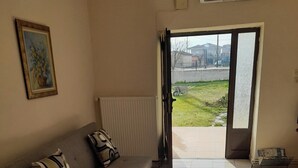 A living room with a sofa, a patterned rug, a radiator, and a view through an open door to the outside. - Garden Paradise in Megalochori Trikala (Trikala)