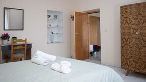 Une chambre d’hôtel comprenant un lit, une armoire en bois, un bureau avec une chaise, une étagère avec des objets décoratifs et un miroir.