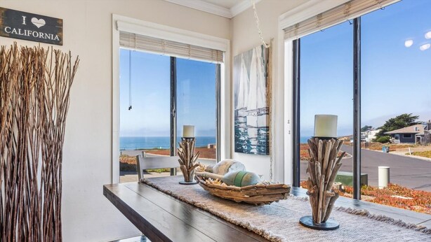 A room with a wooden table, a bowl with decorative items, and two floor lamps. A large window offers a view of the ocean and a road. - Quick walk to the Beach
3 Bedrooms 1.5 Bath
 Sleeps 6 (Dillon Beach)