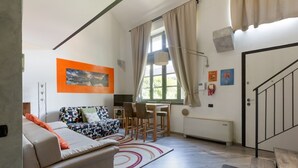 Una sala de estar con un sofá, una mesa de comedor con sillas, un ventanal con cortinas y una escalera.