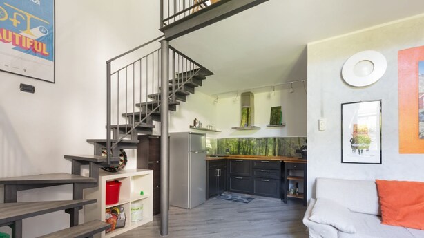 Una cocina moderna con una escalera, un comedor con bancos y un salón con sofá.
