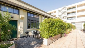 Un edificio moderno con techo plano, ventanas amplias y una zona de estar exterior cubierta con una mesa y sillas.