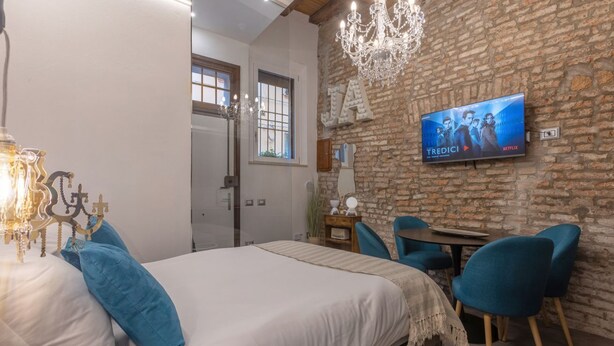 A bedroom with a bed, a TV on the wall, a chandelier, and a desk with chairs. - GuestHost - Ferrara Jungle Apartment (Ferrara)