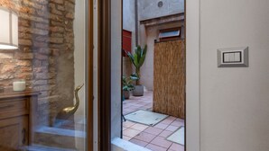 A glass door leading to a courtyard with a brick wall, a lamp, a plant, and a switch on the wall. - GuestHost - Ferrara Jungle Apartment (Ferrara)