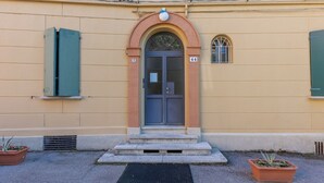 Um edifício com entrada central, uma pequena janela acima da porta e o número '44' na parede.