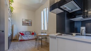 Um espaço de estar compacto com cozinha compacta, um sofá com almofadas estampadas, uma mesa de jantar e uma janela com cortinas.
