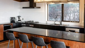Una cucina moderna con una grande isola, sgabelli da bar e vista sugli alberi attraverso una finestra.