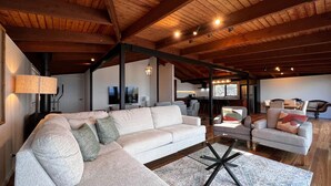 Un ampio soggiorno con un grande divano componibile, un tavolino in vetro e un soffitto in legno.