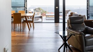 Un interno moderno con soffitto in legno, zona pranzo con sedie e tavolo, divano in pelle e tavolino in vetro con base nera.
