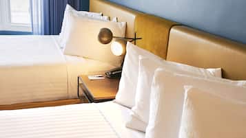 A hotel room with two beds, a bedside table with a lamp, and a window with curtains.