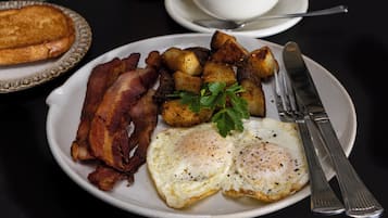 A breakfast plate with bacon, eggs, and potatoes, a cup of coffee, and a glass of orange juice on a table.