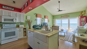A kitchen with white cabinets, a microwave, and a sink. There is a dining area with a table and chairs. - MillionDollarView-Oceanfront 1BR-Updated! (Salter Path)