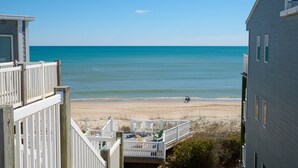 A beach view from a balcony with a wooden deck, a sandy beach, and a clear blue sky. - MillionDollarView-Oceanfront 1BR-Updated! (Salter Path)