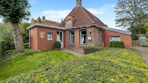 Une maison à deux étages, construite en briques, avec un toit à pignon, une porte d’entrée et un petit jardin à l’avant.