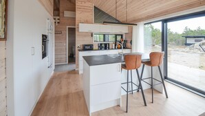 A modern kitchen with a central island, two bar stools, and a large window offering a view of the outdoors. - 3 bedroom lovely home in Anholt (Anholt)