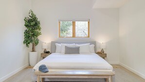 A bedroom with a bed, bedside tables, a window, a plant, and a bench.