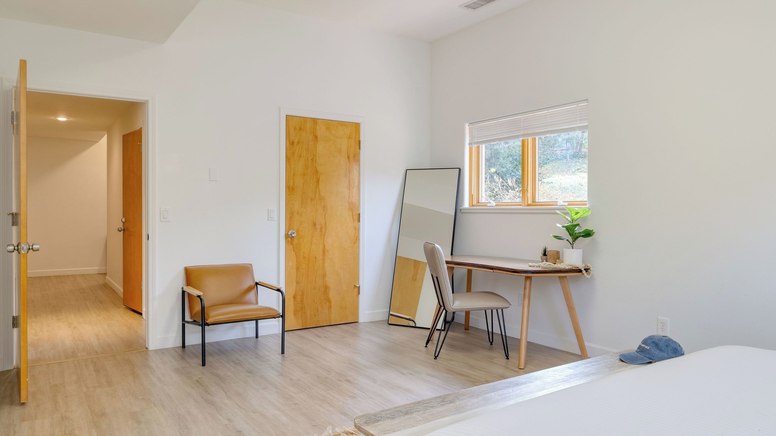 Una habitación con una cama, un escritorio con silla, un espejo y una ventana con persianas.