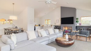 A modern living room with a sectional sofa, a coffee table, a fireplace, a dining area, and a kitchen.