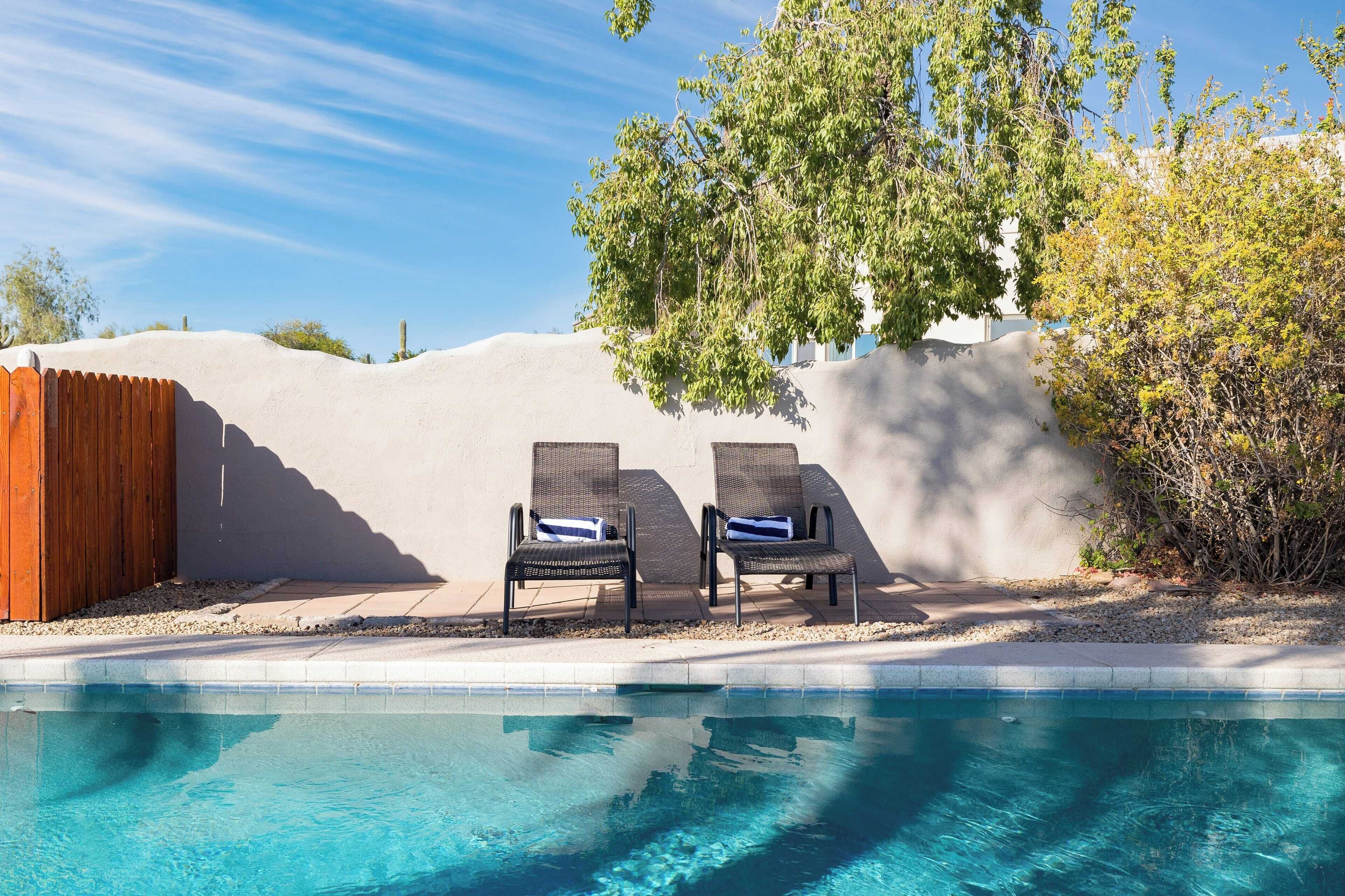 A swimming pool with two lounge chairs and a wooden fence.