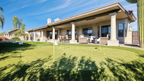 Une maison avec un patio couvert, une pelouse parsemée de balles de golf et un cactus.