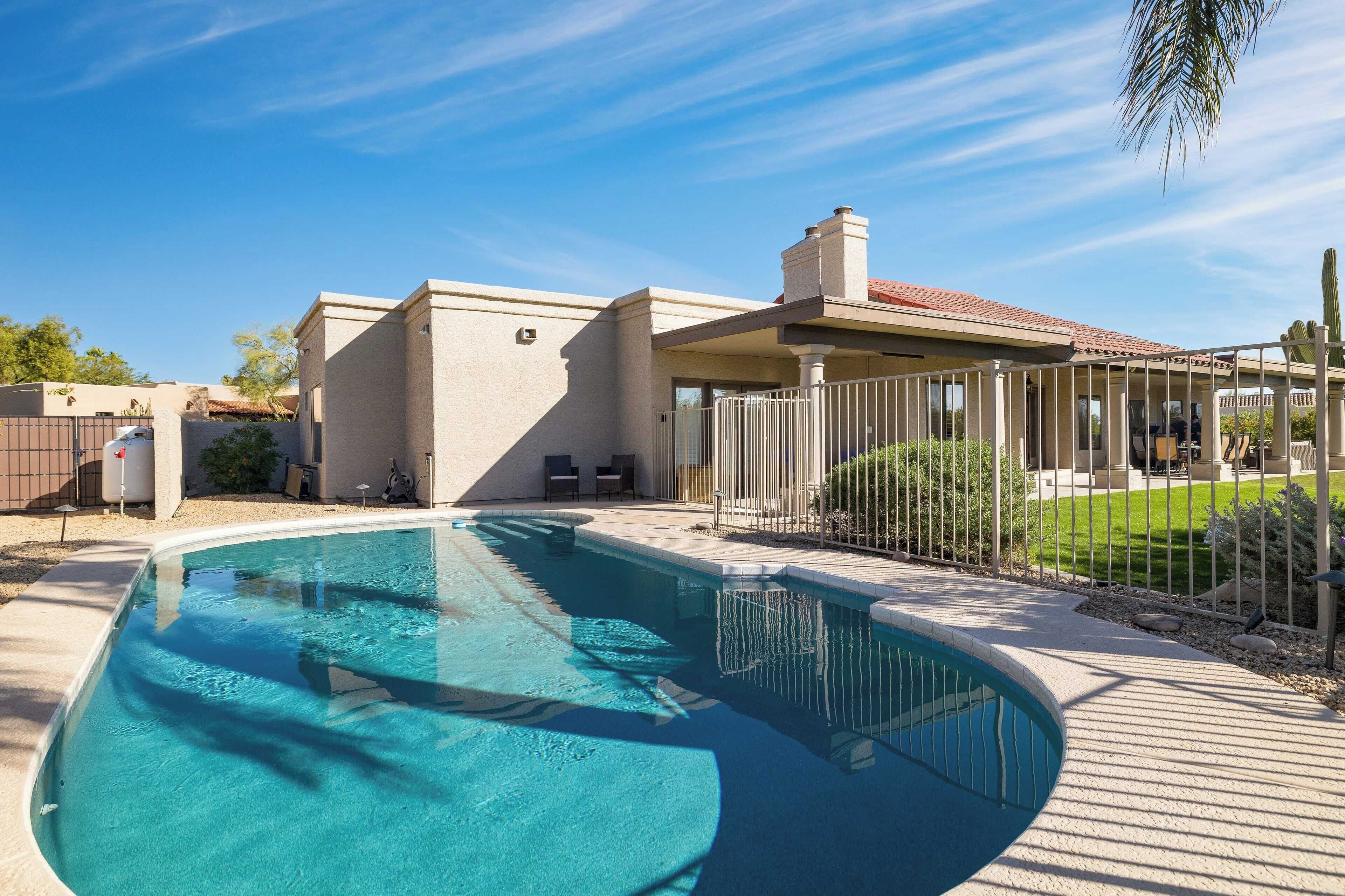 Una piscina con zona de patio, un área de estar cubierta y un jardín vallado.