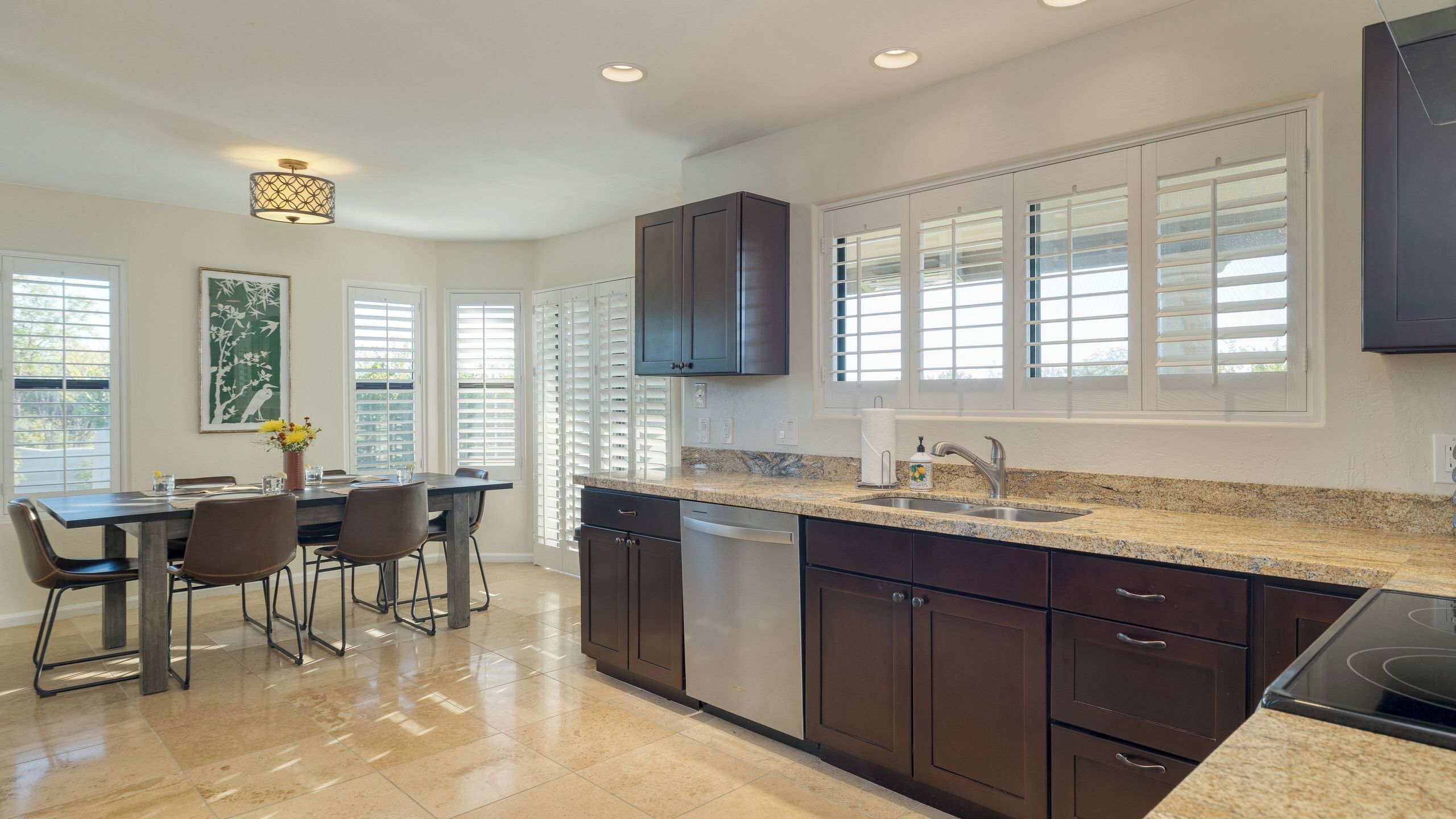A modern kitchen with dark cabinetry, a granite countertop, and a dining area with a table and chairs.