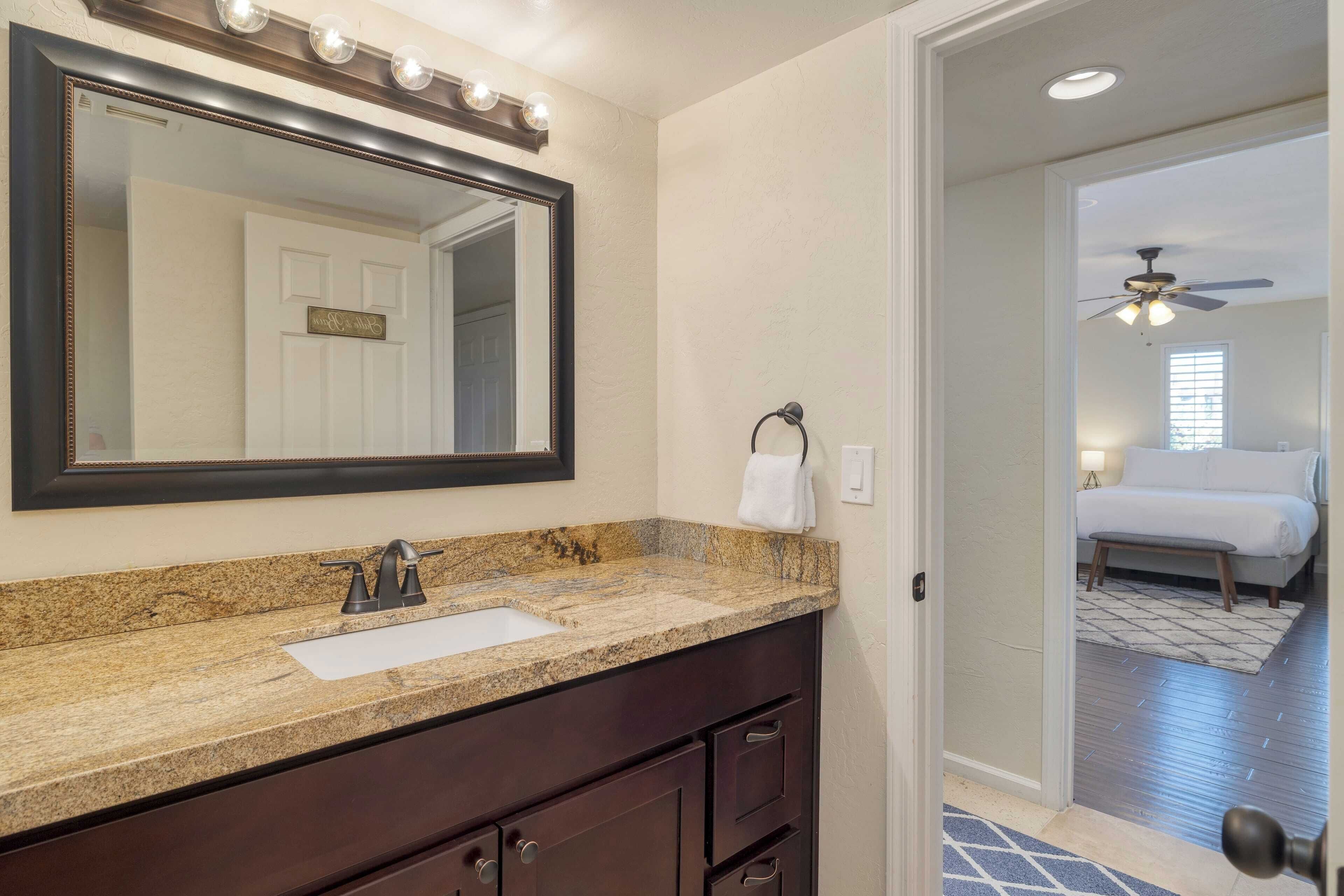 A bathroom with a granite countertop, a sink, a large mirror, and a towel hanging on a ring.