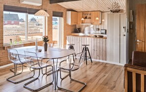 Une cuisine moderne avec des meubles en bois, un coin repas doté d’une table et de chaises en verre, et une vue sur l’extérieur.