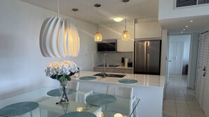 Une cuisine moderne dotée d’un îlot central, d’appareils électroménagers en acier inoxydable et d’un coin repas avec des tables et des chaises en verre.